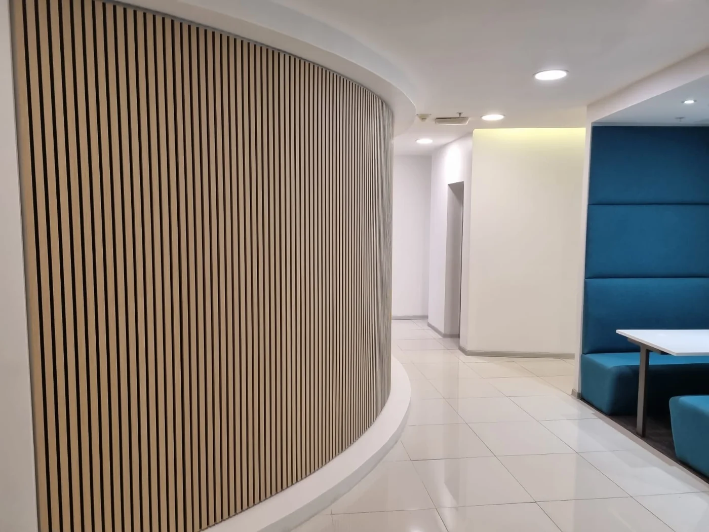 Detalle de un muro curvo revestido con listones de madera en un pasillo de oficina.