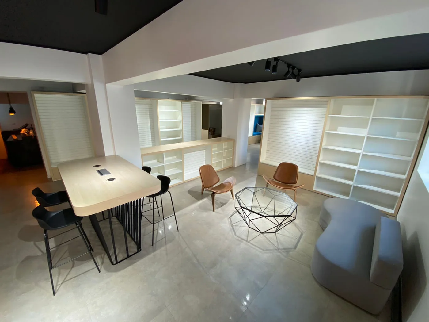 Mesa compartida, sillas y estanterías blancas en un ambiente de oficina.