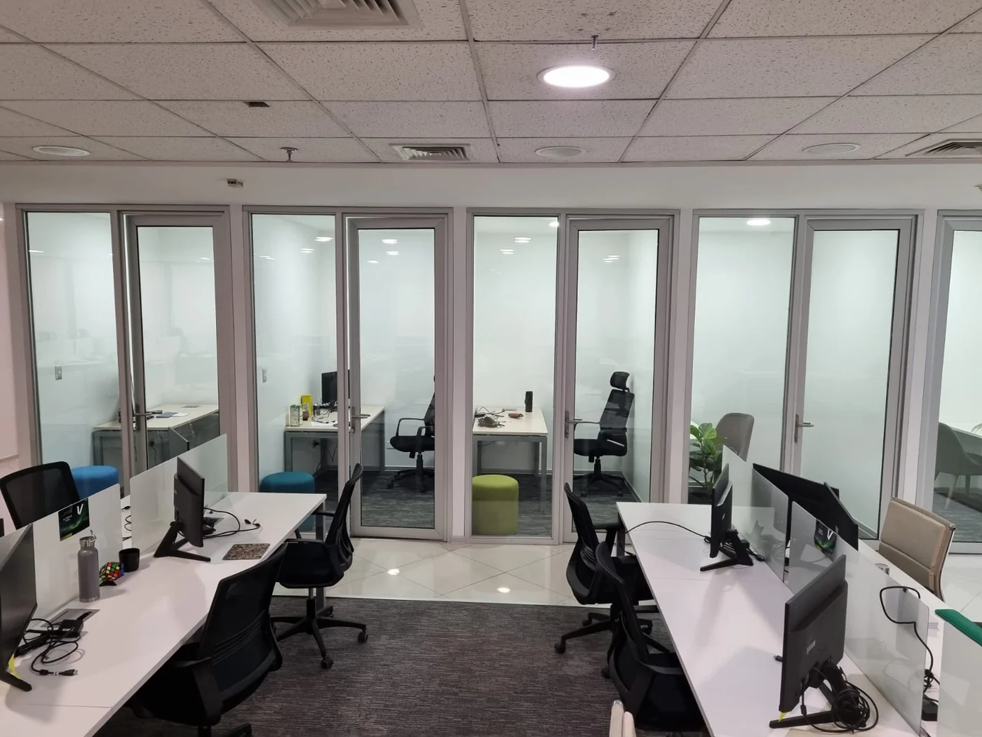 Área de trabajo con escritorios, sillas y recintos separados por mamparas de vidrio.
