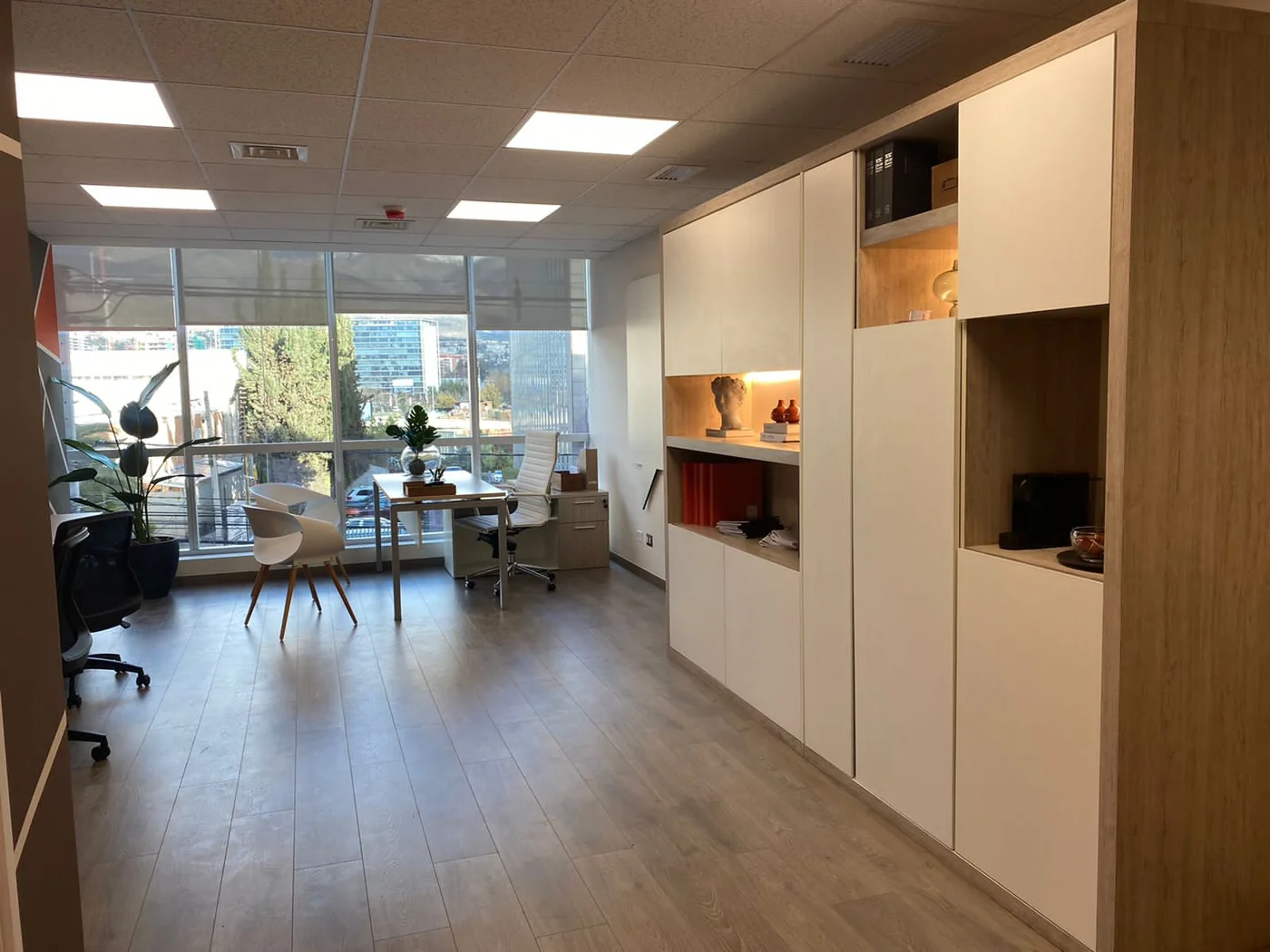 Área de oficina con muebles de guardado blancos y de madera y puestos al fondo.