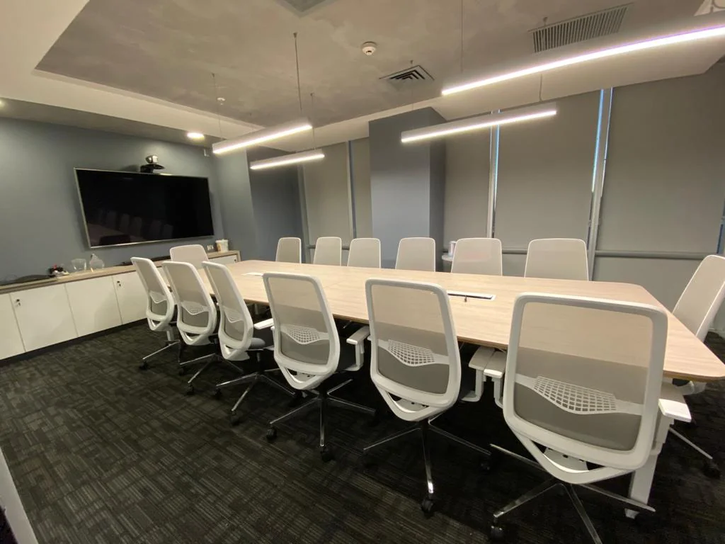 Sala de reunión con mesa clara y sillas de respaldo blanco.