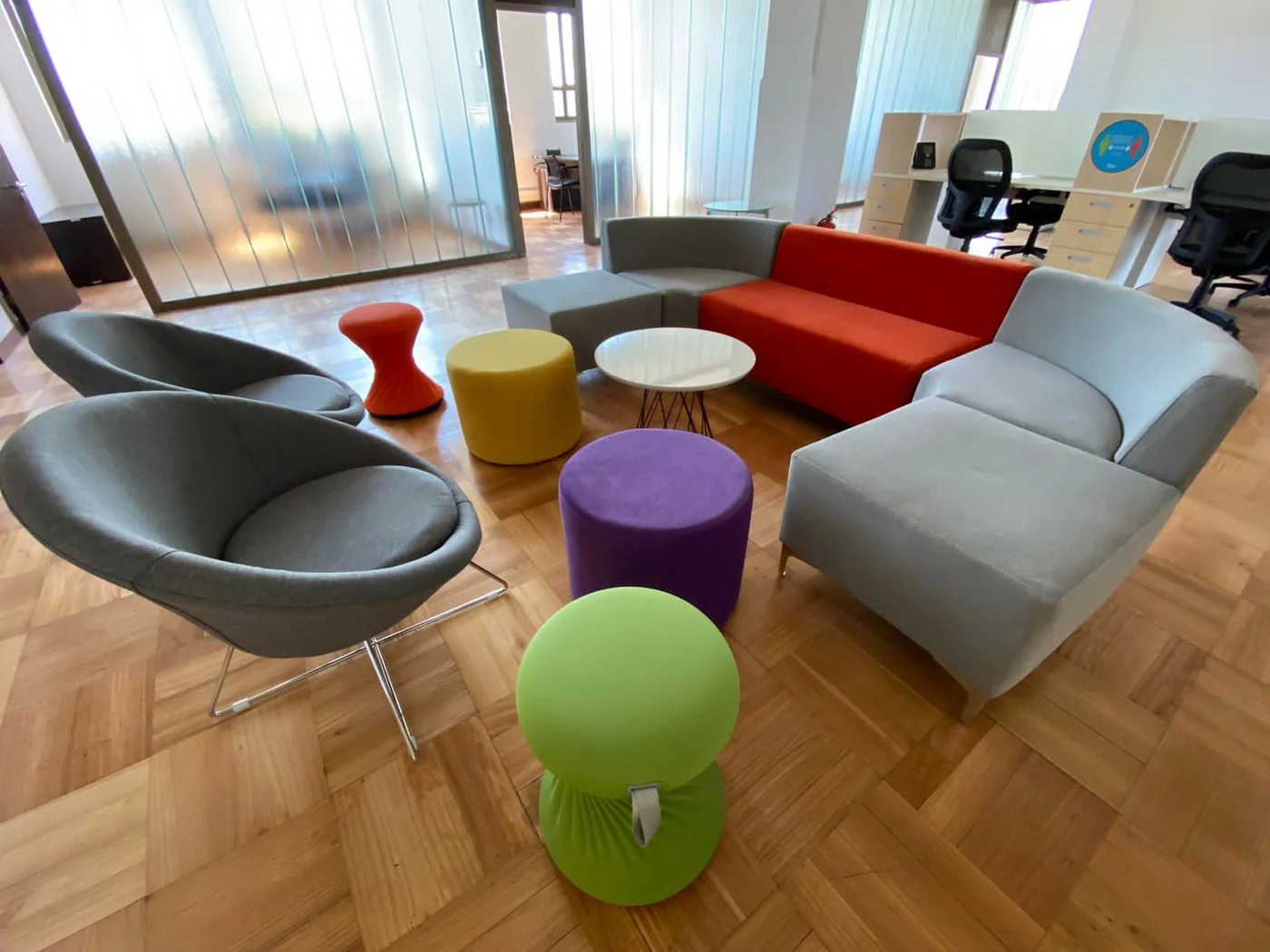 Sillones grises y rojos con mesas auxiliares de colores en un espacio de encuentro.